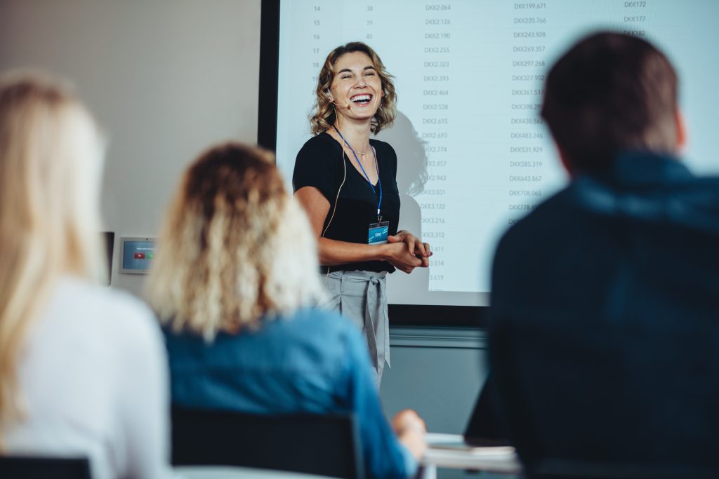 Businesswoman standing at projector screen and smiling during a presentation. Successful female entrepreneur delivering a speech at conference.