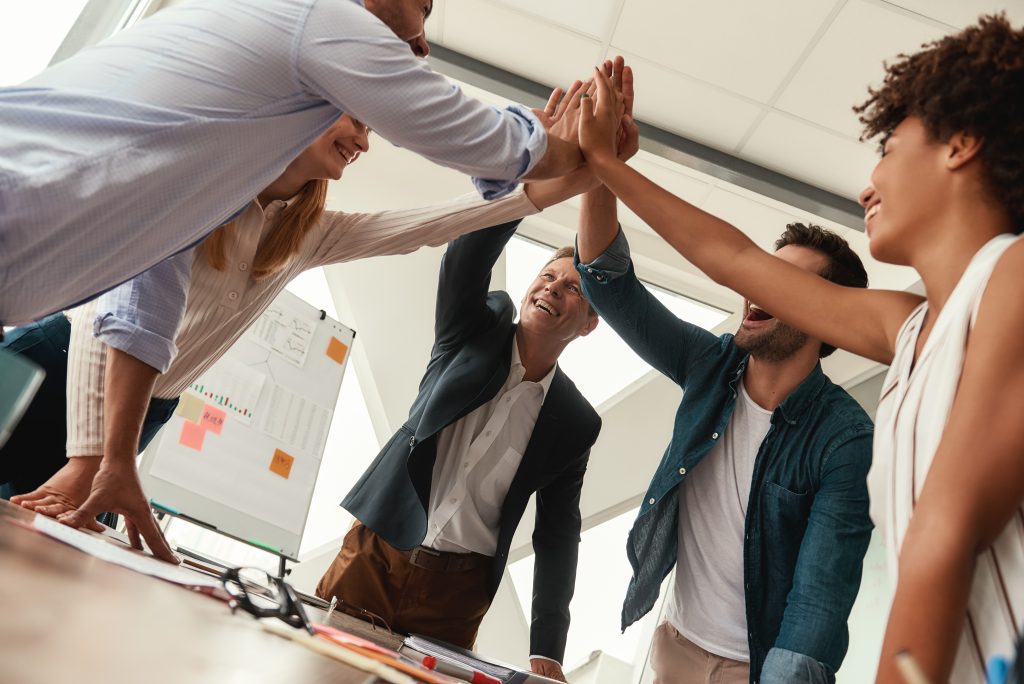 Team giving each other high-five and smiling while working together in the modern office. Teamwork. Success