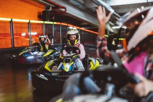 Drivers in helmets racing go-karts on an indoor track, one raising both arms in celebration
