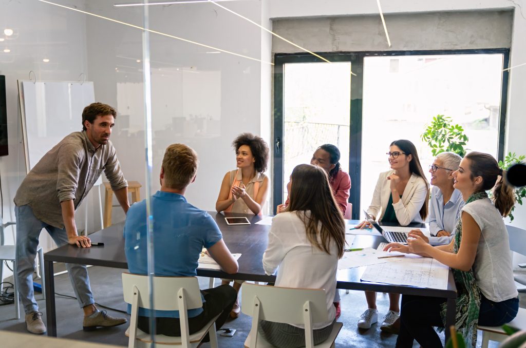 Smiling diverse colleagues gather in boardroom brainstorm discuss financial statistics together, happy multiracial coworkers have fun cooperating working together at office meeting, teamwork concept