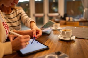 Zwei Personen in Besprechung mit einem Tablet auf dem Tisch und Kaffee.