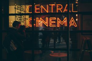 Orange neon sign reading Central Cinema glowing above a darkened cinema entrance at night