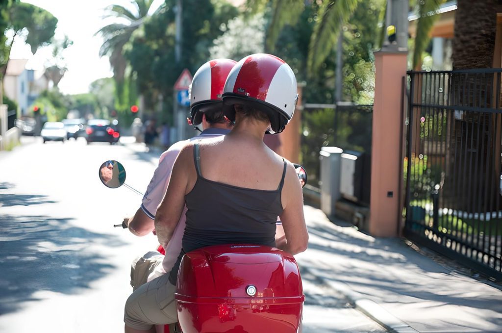 Two people on a vespa on the road in Italy.