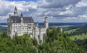 Neuschwanstein Castle with its white towers on a wooded hillside above the Bavarian plain