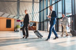 One Woman and two men in business outfits in a entrance hall with suitcase.