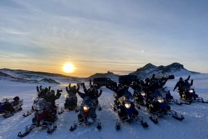 Group of people with snowmobiles, sunset.
