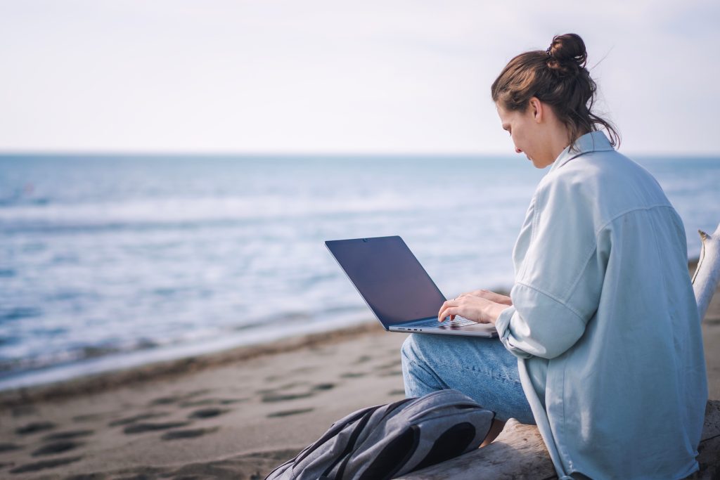 Yong woman sitting on the beach with a laptop working.