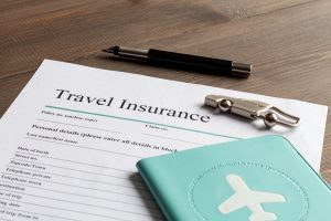 Travel insurance document on wooden table with pen and passport.