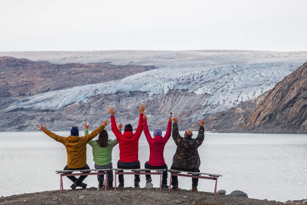 Group of people sitting on a bench in front of lake, glacier in Iceland.