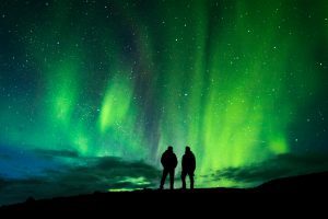 Northern lights in Iceland, two people standing under the dark sky and watching the lights.