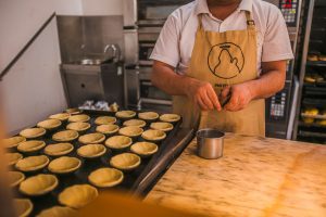 Men making pastel de nata in bakery.