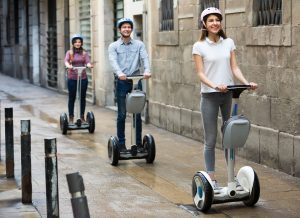 Two women and a man with helmets ride through the city on Segways.