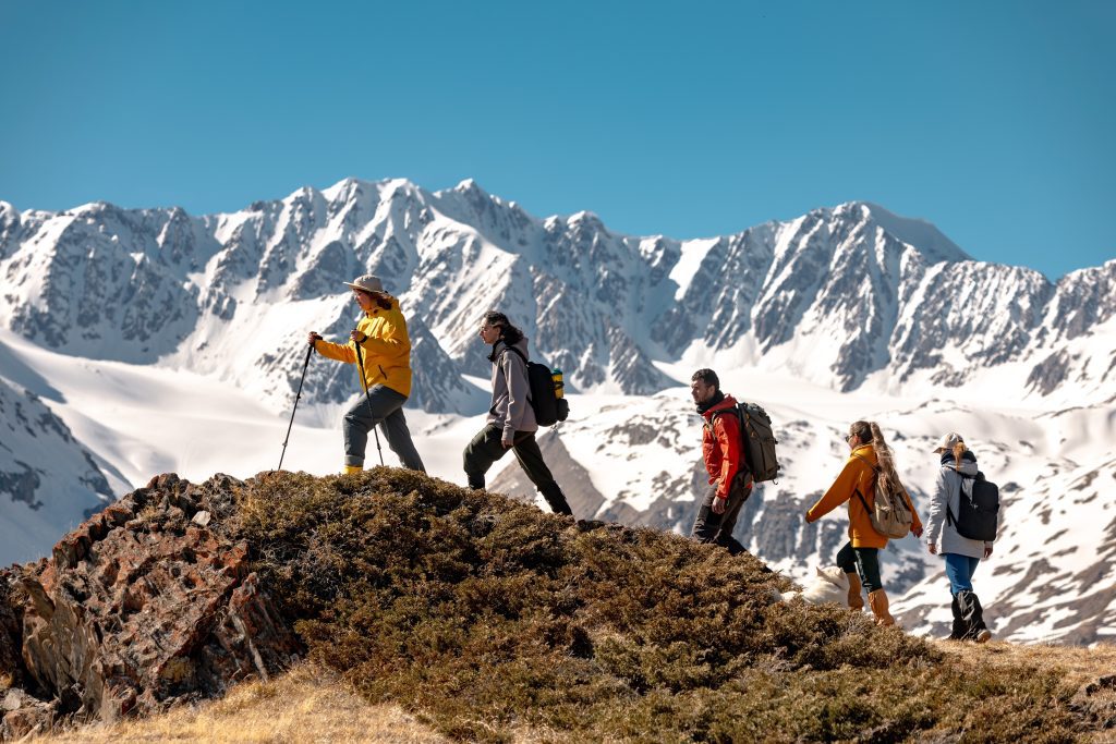 Group of people hiking up a mountain, snow in the background and blue sky.