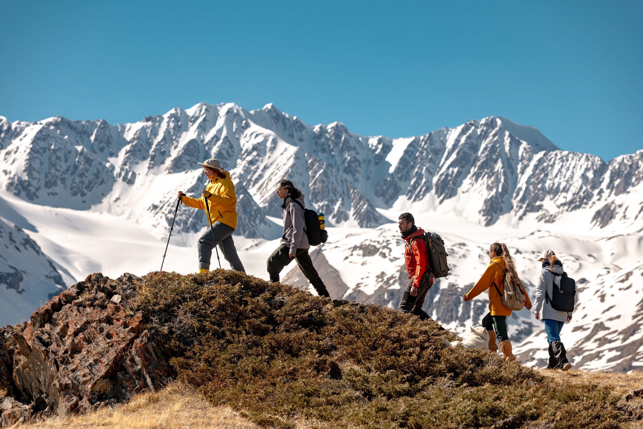 Gruppenwanderung auf den Berg mit Schnee im Hintergrund und blauer Himmel.