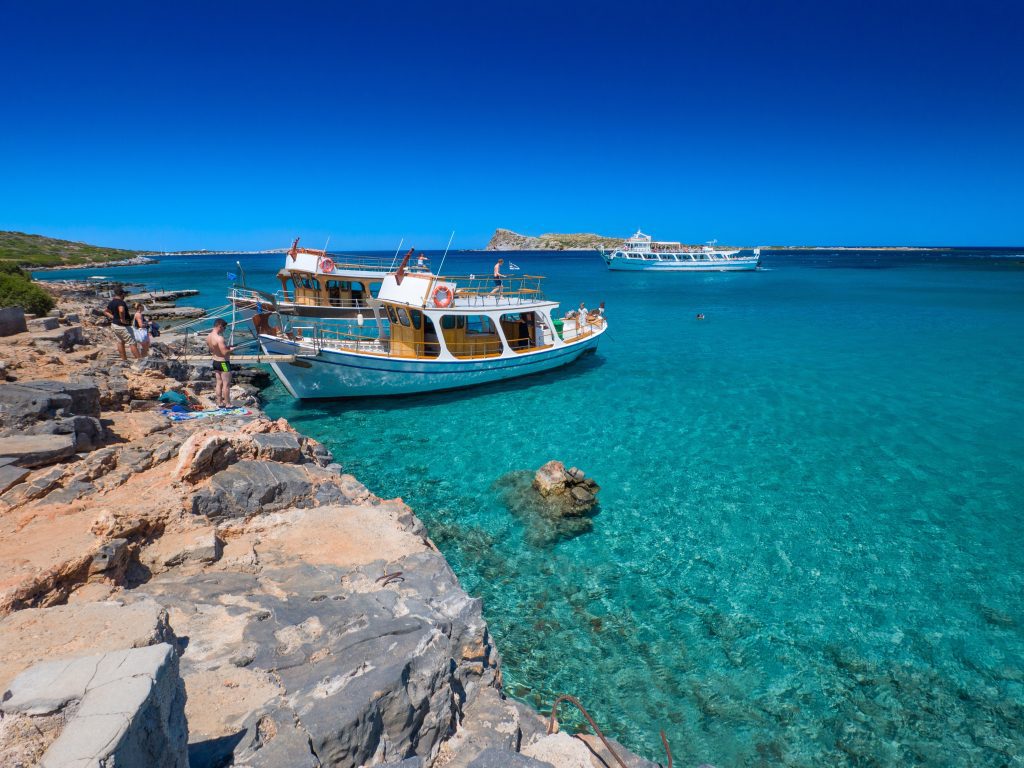 Two boats close to the shore in Crete, floating on crystal-clear turquoise water and surrounded by a peaceful Mediterranean coastal landscape.