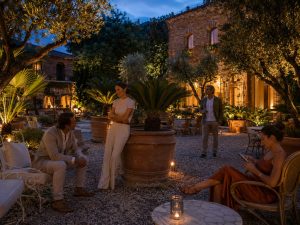Guests seated at tables on a lantern-lit garden terrace beside a stone hotel building