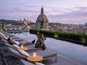 Hotel terrace with sun loungers and a pool overlooking the Barcelona skyline at sunset