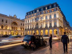 Illuminated facade of a luxury hotel in central Lisbon at dusk, with a car and guests at the entrance