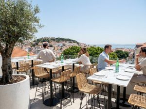 Rooftop bar terrace in Lisbon with dining tables and potted plants overlooking the city