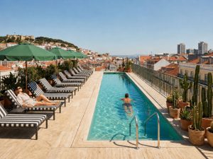Rooftop pool with white sun loungers and a panoramic view over Lisbon, with a swimmer in the water