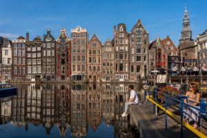 Row of narrow gabled canal houses in Amsterdam with boats moored along the quayside