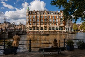 Grand historic canal-side building in Amsterdam with turrets and arched windows, seen across the water