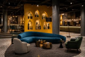 Boutique hotel lounge with a curved teal banquette, dark panelled walls and gold-lit display niches