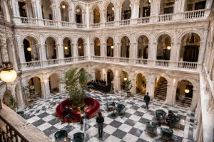 Hotel restaurant in a glass-roofed atrium with arcaded galleries, a chequerboard floor and tables set with red flowers