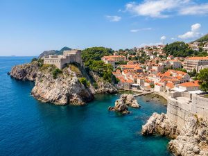 Stone village with terracotta roofs on a rocky promontory, surrounded by clear blue Adriatic water and pine woodland