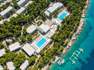 Aerial view of a low-rise Croatian coastal resort with outdoor pools, set among pine woodland on a peninsula