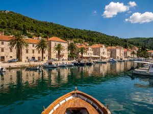 Croatian coastal town of stone buildings and terracotta roofs along a harbour, with wooded hills rising behind