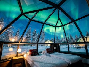Bed inside a glass igloo with the Northern Lights visible through the transparent dome
