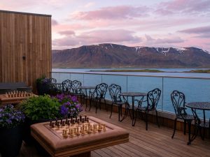 Wooden restaurant terrace with dining tables overlooking a lake and mountains at sunset in Iceland