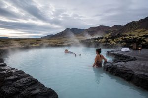 Steaming geothermal bathing pool set in dark volcanic rock under an overcast Icelandic sky