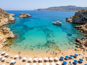 Sandy Maltese cove with rows of blue parasols and sun loungers beside clear turquoise water and rocky cliffs