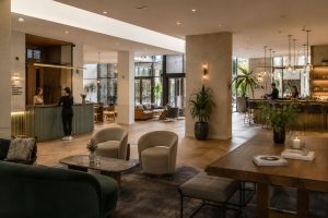 Bright hotel lobby lounge with light wood panelling, potted palms and armchairs beside the reception desk