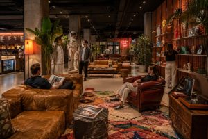 Hotel lounge with patterned armchairs, framed artwork, bookshelves and warm lamp lighting